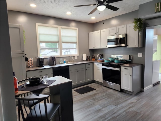 kitchen with light hardwood / wood-style flooring, appliances with stainless steel finishes, sink, ceiling fan, and a textured ceiling