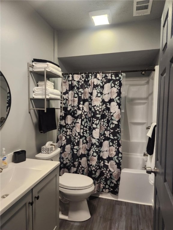 full bathroom featuring hardwood / wood-style floors, toilet, vanity, shower / bath combo with shower curtain, and a textured ceiling