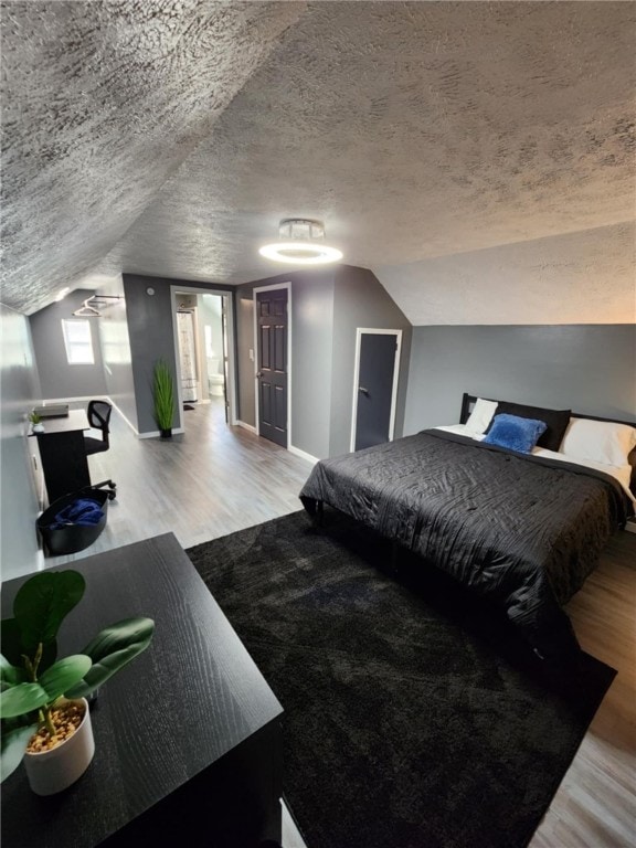 bedroom with vaulted ceiling, a textured ceiling, and hardwood / wood-style floors