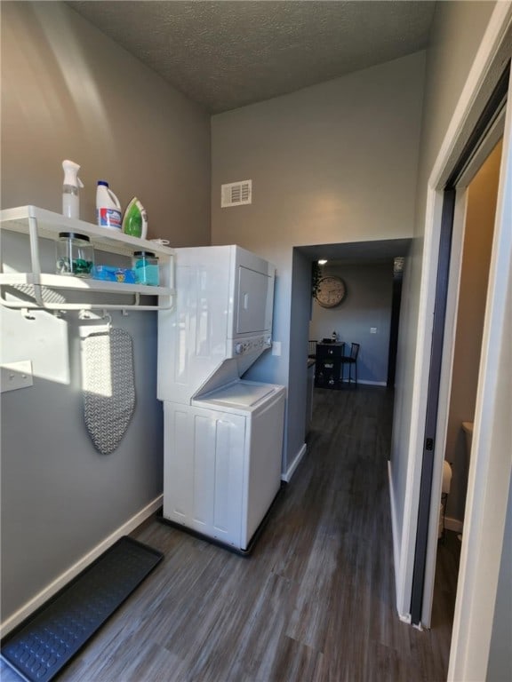 washroom with dark wood-type flooring, stacked washer and dryer, and a textured ceiling