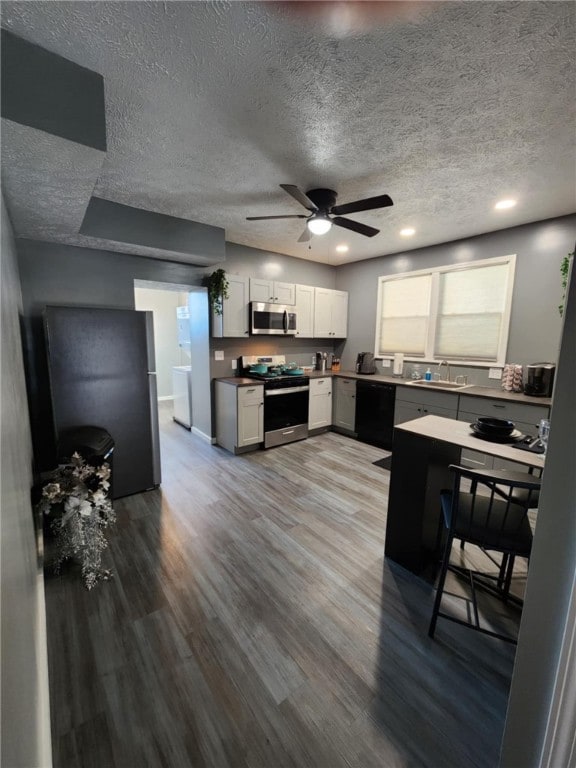 kitchen featuring stainless steel appliances, white cabinetry, wood-type flooring, ceiling fan, and a textured ceiling