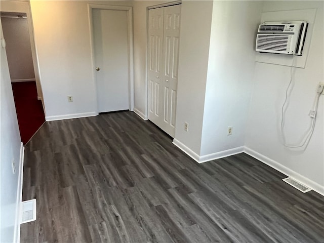 unfurnished bedroom with a wall mounted AC and dark hardwood / wood-style flooring