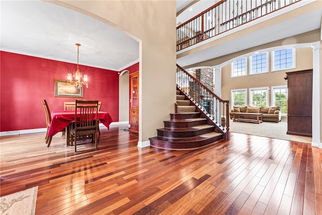 interior space featuring wood-type flooring, ornate columns, crown molding, and a high ceiling