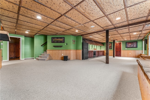 basement with black refrigerator, carpet, and wooden walls