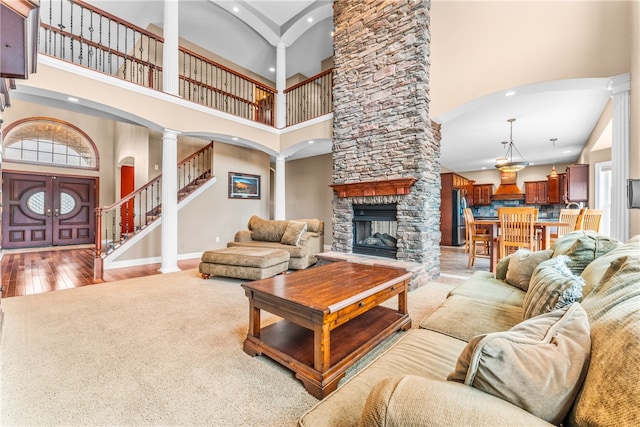 living room featuring a fireplace, a high ceiling, light wood-type flooring, and ornate columns