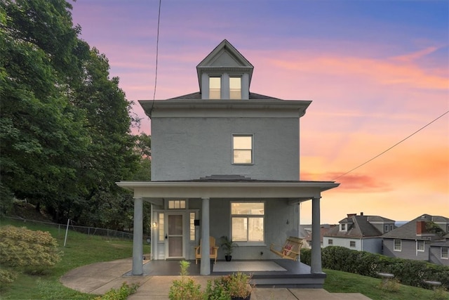 back house at dusk with a yard and covered porch