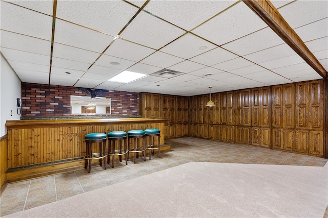 interior space with a drop ceiling, wooden walls, bar, and carpet flooring