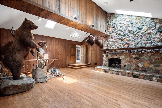 living room with light hardwood / wood-style floors, a skylight, wood walls, and a stone fireplace