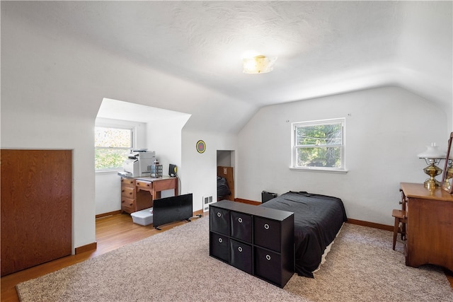 bedroom featuring multiple windows, light wood-type flooring, and vaulted ceiling