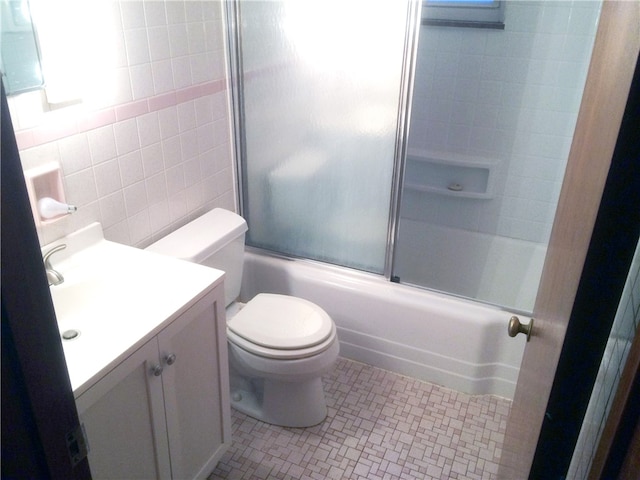 full bathroom featuring tile walls, vanity, combined bath / shower with glass door, tile patterned flooring, and toilet