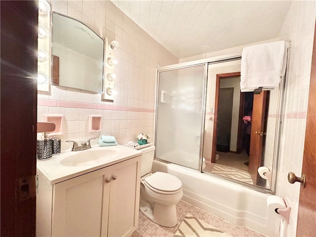 full bathroom featuring shower / bath combination with glass door, vanity, tile patterned floors, tile walls, and toilet