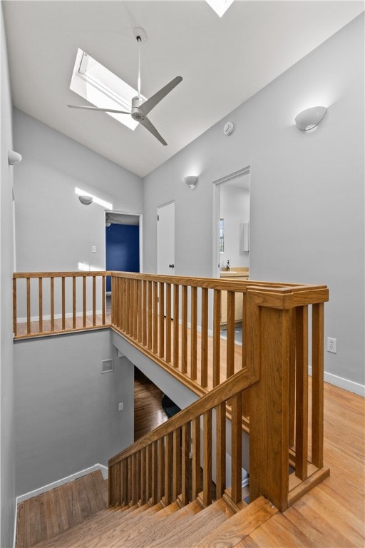 stairs with wood-type flooring, a skylight, and ceiling fan