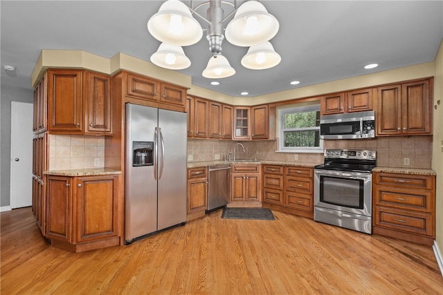 kitchen featuring appliances with stainless steel finishes, light hardwood / wood-style flooring, light stone countertops, and hanging light fixtures