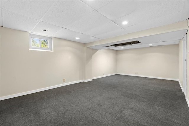 basement with a paneled ceiling and dark colored carpet