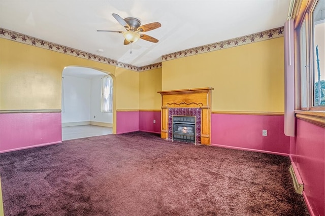 unfurnished living room with a baseboard heating unit, carpet flooring, ceiling fan, and a tiled fireplace