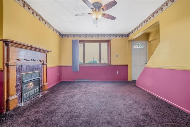 unfurnished living room featuring baseboard heating, ceiling fan, a fireplace, and dark colored carpet