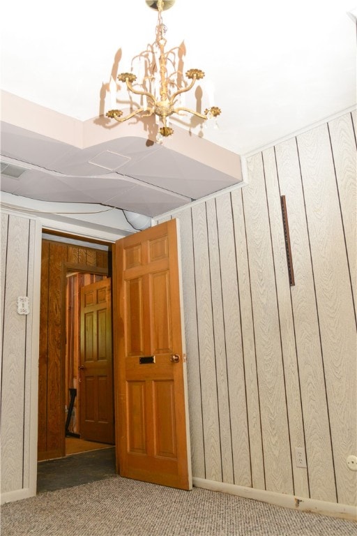 stairs with a notable chandelier, wooden walls, and carpet flooring