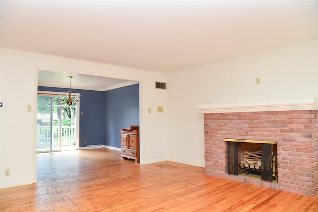 unfurnished living room with a brick fireplace, ornamental molding, a notable chandelier, and hardwood / wood-style floors