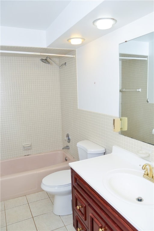 full bathroom with tile walls, tile patterned floors, vanity, tiled shower / bath, and toilet