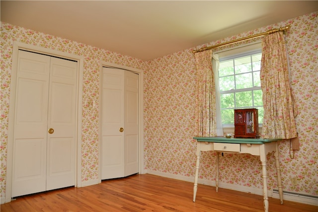 unfurnished bedroom featuring baseboard heating, two closets, and hardwood / wood-style floors