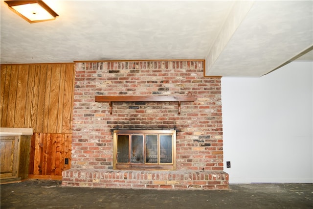 unfurnished living room with concrete flooring, wooden walls, and a fireplace