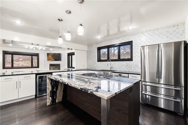 kitchen featuring dark stone countertops, backsplash, beverage cooler, a center island, and appliances with stainless steel finishes