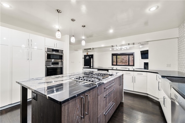 kitchen with white cabinets, a center island, decorative light fixtures, appliances with stainless steel finishes, and dark hardwood / wood-style floors