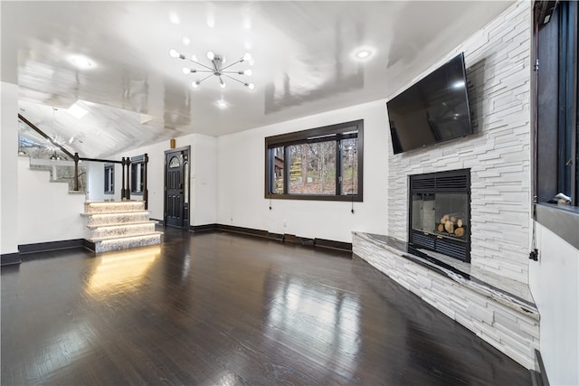 unfurnished living room with lofted ceiling, dark wood-type flooring, an inviting chandelier, and a fireplace