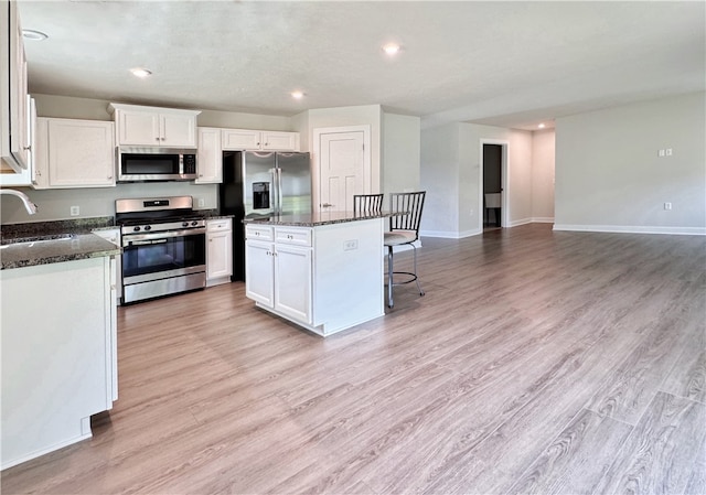 kitchen with stainless steel appliances, sink, white cabinetry, and light hardwood / wood-style floors