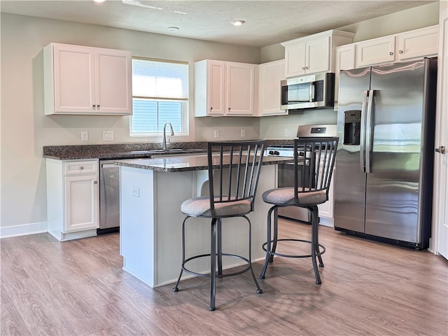 kitchen with light wood-type flooring, white cabinetry, stainless steel appliances, a kitchen island, and a breakfast bar area