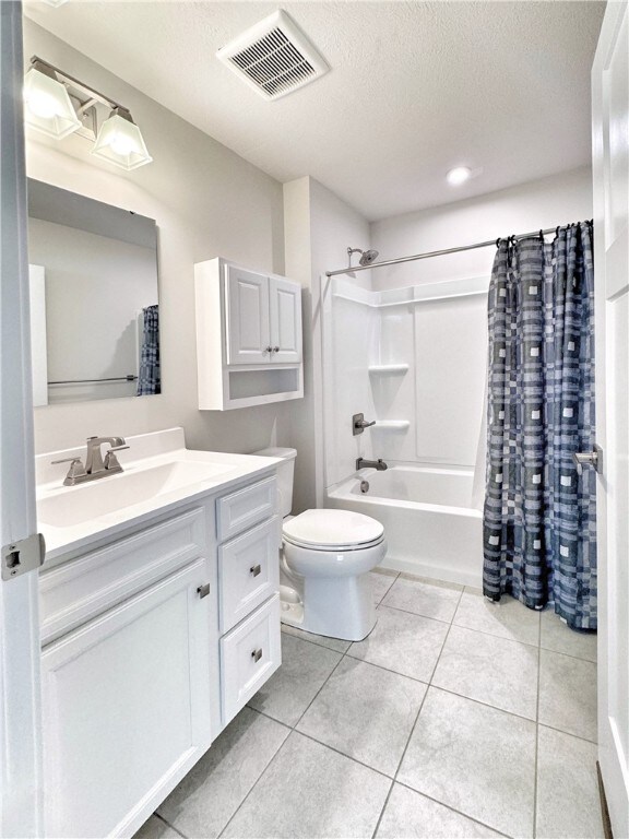 full bathroom featuring toilet, tile patterned floors, vanity, a textured ceiling, and shower / bath combination with curtain