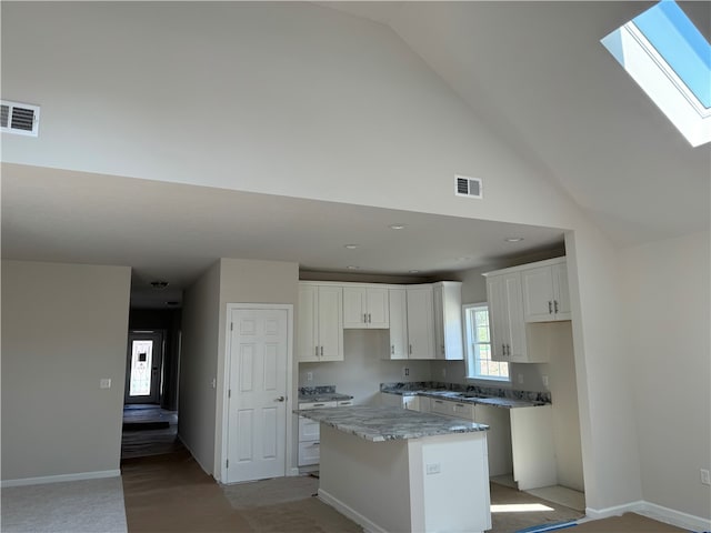 kitchen featuring high vaulted ceiling, white cabinetry, a skylight, a kitchen island, and light stone counters