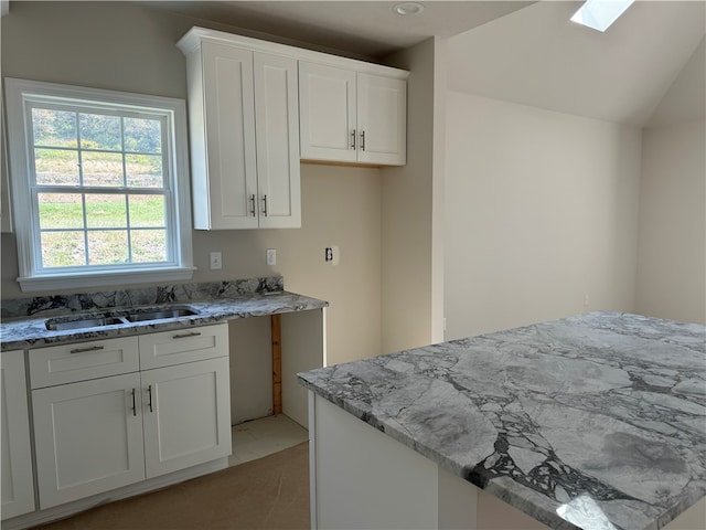 kitchen with vaulted ceiling with skylight, light stone counters, white cabinetry, and sink