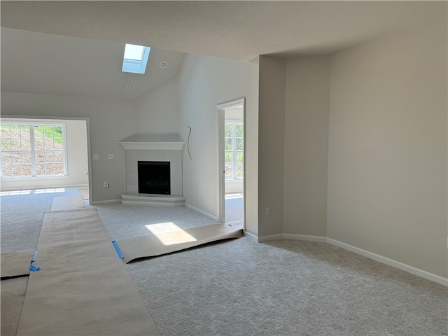 unfurnished living room with vaulted ceiling with skylight, a tile fireplace, plenty of natural light, and carpet