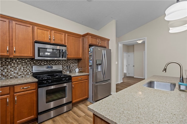 kitchen featuring vaulted ceiling, light wood-type flooring, stainless steel appliances, sink, and tasteful backsplash