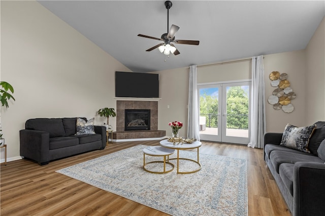 living room featuring a tiled fireplace, french doors, vaulted ceiling, wood-type flooring, and ceiling fan