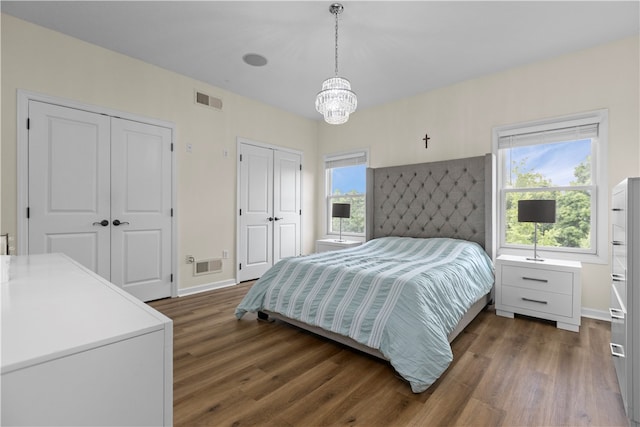 bedroom with two closets, dark hardwood / wood-style floors, and a chandelier