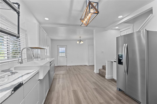 kitchen featuring light wood finished floors, stainless steel appliances, white cabinets, a sink, and baseboards