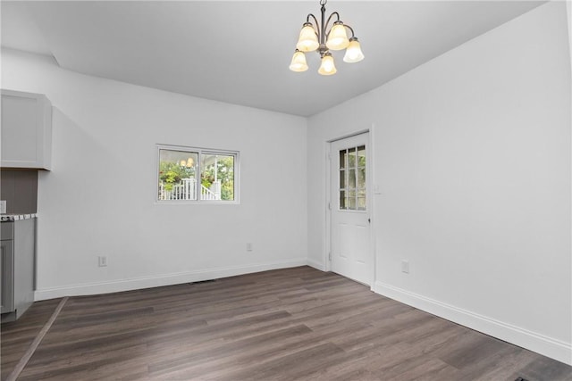 unfurnished dining area featuring dark wood-type flooring, a notable chandelier, and baseboards