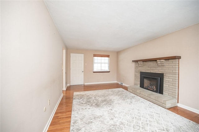 unfurnished living room with wood-type flooring and a brick fireplace