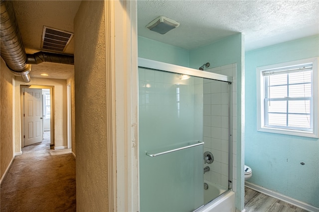 bathroom featuring hardwood / wood-style floors, toilet, combined bath / shower with glass door, and a textured ceiling