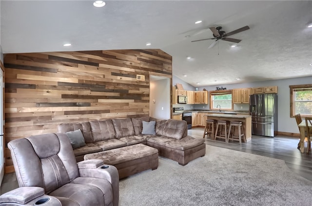 living room with vaulted ceiling, wood walls, wood-type flooring, and ceiling fan