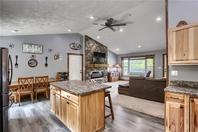 kitchen with dark wood-type flooring, a stone fireplace, a textured ceiling, and vaulted ceiling