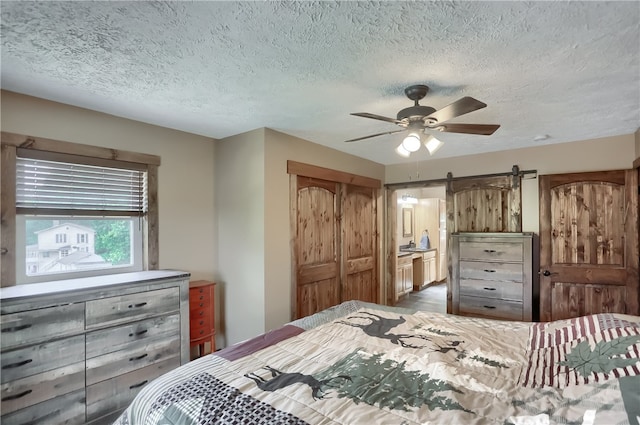 bedroom featuring a textured ceiling, ceiling fan, and a barn door