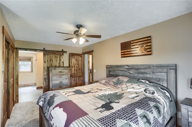 bedroom featuring a textured ceiling, a barn door, ceiling fan, and light colored carpet