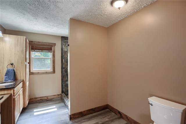 bathroom featuring hardwood / wood-style floors, walk in shower, toilet, vanity, and a textured ceiling