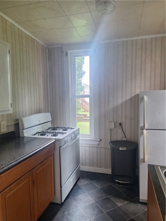 kitchen with a wealth of natural light, white appliances, and dark tile patterned flooring