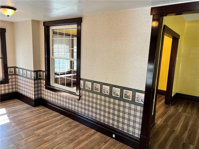 unfurnished room featuring baseboards, wood finished floors, and wallpapered walls