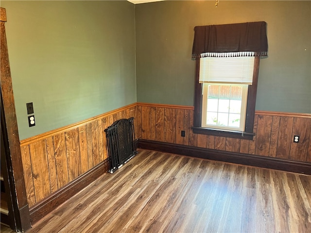 unfurnished room featuring radiator heating unit, wood-type flooring, and wooden walls