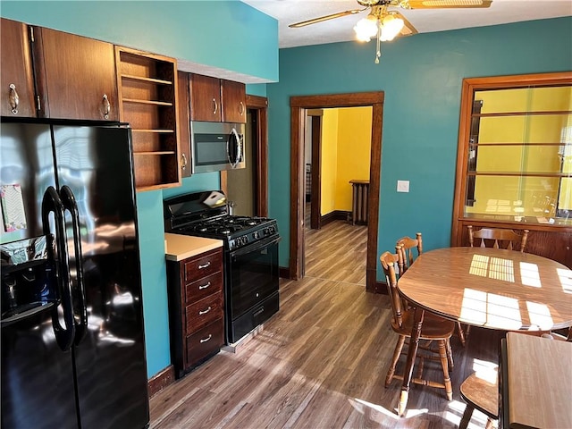 kitchen with dark wood-style flooring, open shelves, light countertops, black appliances, and baseboards